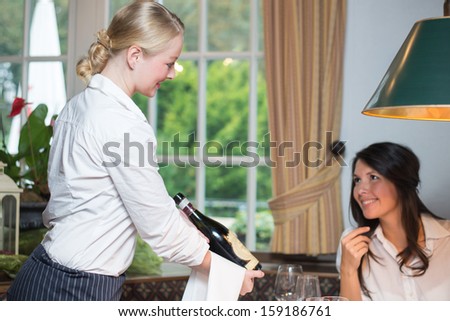 Young waitress showing wine bottle to female client and waiting for the client approval in a fine dinning restaurant