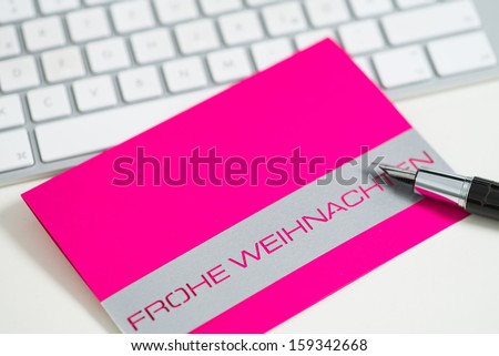 Blank vivid pink Christmas tag or card with the words - Frohe Weinachen - or Merry Christmas lying on a computer keyboard with an open fountain pen to write your message or seasonal greeting
