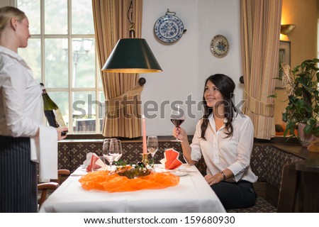 Waiter serving red wine in a fine dining restaurant with happy female customer sitting at table