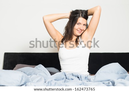 Healthy woman refreshed after a good nights sleep stretching in bed and smiling at the camera in pleasure and satisfaction