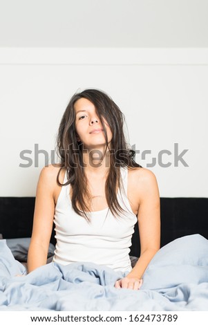 Tired young woman waking up after a nights sleep giving the camera a lazy smile as she sits in her bed in her sleepwear trying to motivate herself, with copy space