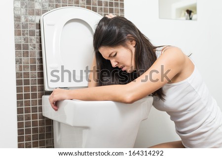 Young woman vomiting into the toilet bowl in the early stages of pregnancy or after a night of partying and drinking