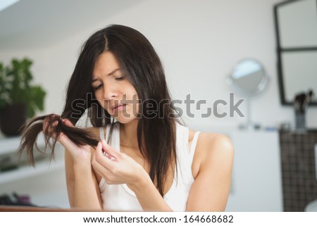 Horrified young woman looking in the bathroom mirror staring open mouthed at the first grey hair on her scalp, a first sign of aging, or noticing that she is suffering from dandruff