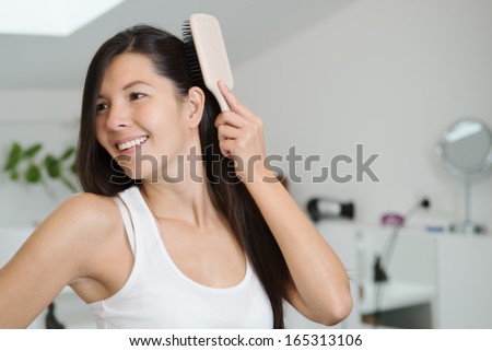Attractive woman brushing her hair looking at the camera with a friendly charming smile
