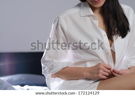 Young woman unbuttoning her white shirt as she prepares to go to bed in the evening with a tantalizing glimpse of her bra visible