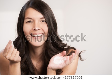 Happy attractive woman applying face cream or moisturizer which she is displaying on the palm of her hand as she uses her finger to apply it to her skin in a skincare and beauty concept