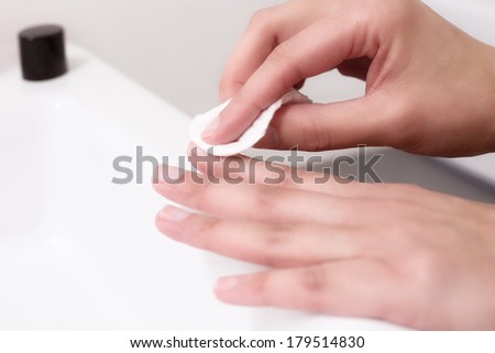 Woman removing nail varnish with acetone on a small cotton pad on the edge of a hand basin as she cares for her nails and cuticles in a health and beauty concept