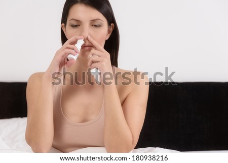 Young woman inhaling nose drops to relieve nasal congestion caused by a cold or an allergy resulting in hay fever