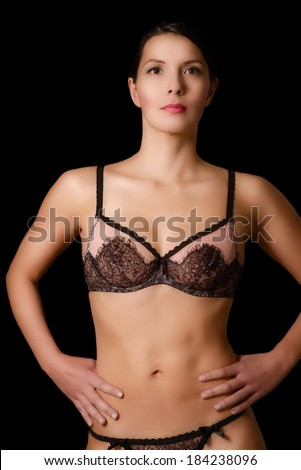 Beautiful sexy young woman with a shapely figure posing in the darkness in lacy black lingerie with her hands on her hips looking at the camera with a serious expression