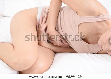 Woman with her monthly menstrual pains clutching her stomach with her hands as she becomes stressed by the ongoing cramps while being in her bed