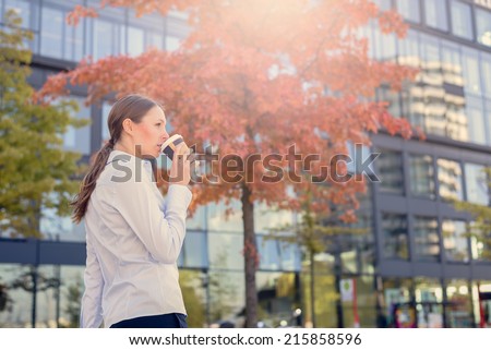 Urban Woman Sipping Coffee in To Go Cup in Autumn City Environment with Sun Shining in Background