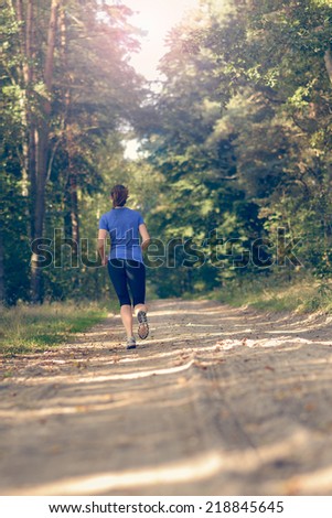 Athletic young woman in sportswear jogging away from the camera along a forest track in a fitness and wellness concept