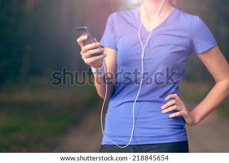 Close up torso view of a woman in a blue blouse standing outdoors listening to music on an MP3 player