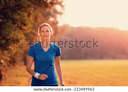 Attractive active young woman out exercising in glowing morning light on a country path through woodland and fields in a health, fitness and zen concept with copy space