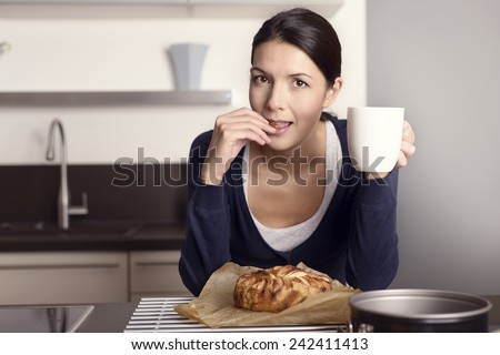 Young woman relaxing in the kitchen with a mug of coffee tasting her freshly baked apple cake
