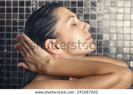 Attractive woman washing her hair in the shower rinsing it off under the spray of water with her head tilted back and eyes closed in a hair care, beauty and hygiene concept