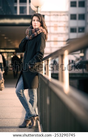 Full Length Shot of Stylish Pretty Young Woman in Autumn Fashion Leaning on Pathway Side Rails, Looking at the Camera.
