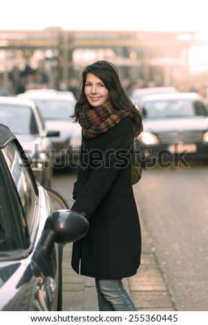Stylish Young Woman in Black Coat and Scarf Opening the Door of her Car Parking at the Street Side While Looking at the Camera.