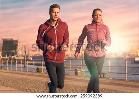 Fit active young couple running on a seafront promenade with the athletic woman leading the way approaching the camera in a healthy lifestyle concept