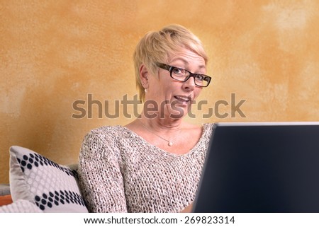 Serious Middle Age Woman with Short Blond Hair Sitting on Sofa While Using her Laptop Computer.