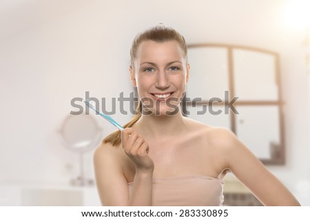 Smiling healthy woman with bare shoulder and a toothy friendly smile holding a toothbrush in her hand conceptual of dentistry, oral hygiene, and prevention of caries