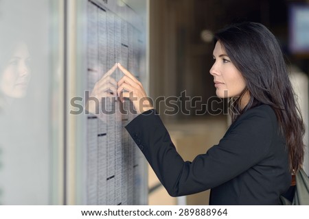 Attractive woman reading the train timetable running down the columns with her finger as she tries to find the right entry, side view