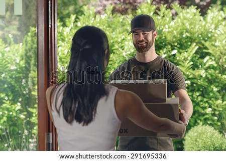 Deliveryman or postman making a door to door delivery handing over a large cardboard box to a housewife, view from behind over her shoulder of the man