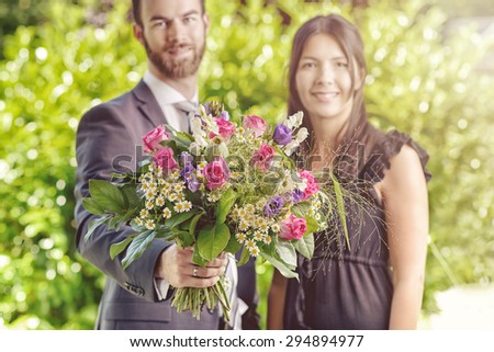 Happy Young Couple at the Garden with Bouquet of Assorted Fresh Flowers, Smiling at the Camera.