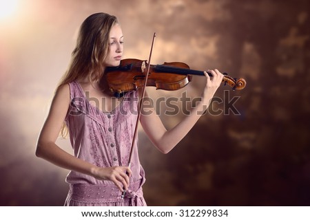 Pretty young female violinist in a stylish pink outfit standing playing the violin as she gives a classical recital at the academy or practices for a performance