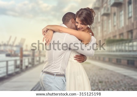 Happy romantic young couple share a special tender moment hugging each other as they show their love and affection, side view three-quarter over grey of a multiracial couple