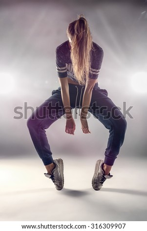 Female Hip Hop Dancer in Tip Toe Position with her Hair Covering her Face Against Brown Wall Background In the Studio.
