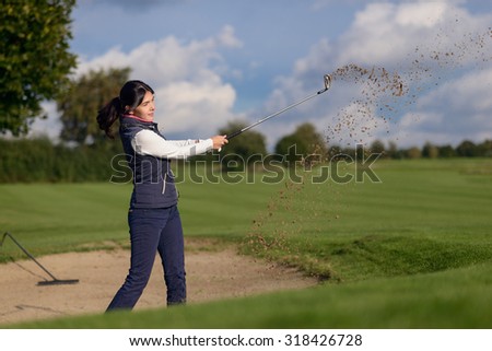 Woman golfer playing out of a sand bunker on a golf course with sand flying from the club as she drives her shot