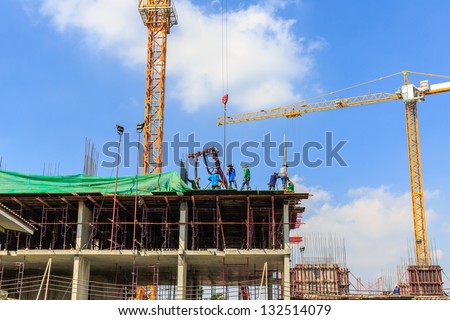 The workers working on a building site along with concrete pump and crane against the white cloud and blue sky
