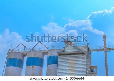 the white smoking chimney of a lime industry against a white cloud and blue sky.