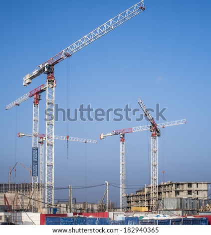 construction cranes begin to build a new residential complex on a blue sky background with industrial smog