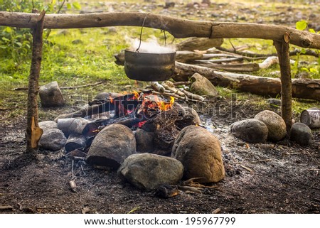 Cooking in a hike in the cauldron hanging over the fire, from the boiler coming white smoke