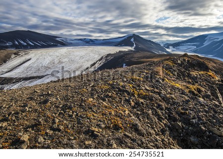 View from the mountain top to the snow-capped peaks illuminated by the rays of the setting sun against the background of dramatic sky near Longyearbyen, Spitsbergen (Svalbard island), Norway