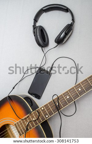 guitar lying on the sofa and lie next to the headphones connected to a mobile phone, the wire from which form the silhouette of a guitarist playing
