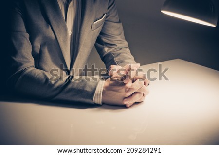close up of a man in a suit with his hands clasped in front
