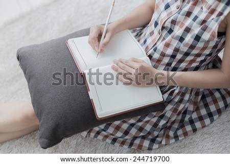 Beautiful young woman writing something in the note pad while lying on the floor at living room