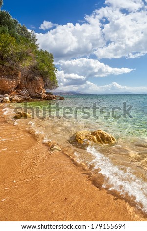 View to tide wave over pebbles and rocks on the sand under transparent water at Ionian sea floor under bright sunlight near Ipsos, Corfu, Greece