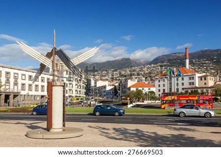 FUNCHAL, MADEIRA, PORTUGAL - NOVEMBER 3 2011: Sculpture standing at Autonomy Square with cars, touristic bus driving. With Funchal city at background.