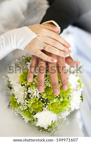 Hands of the newlyweds are on the bride\'s bouquet