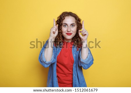 Close-up portrait of surprised young woman pointing with two fingers, looking at camera, isolated on yellow background. Girl in a denim suit nd a red T-shirt Imagine de stoc © 