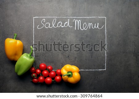 Salad Menu written with chalk on blackboard decorated with fresh tomatoes and peppers