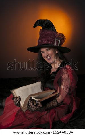 Halloween witch with book of spells on orange background