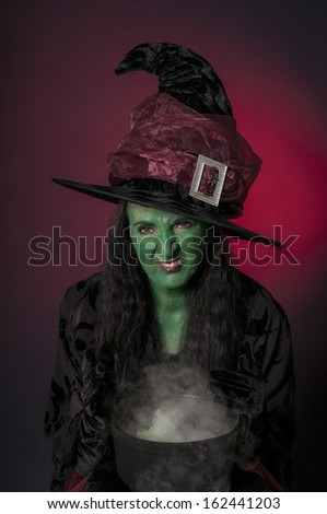Halloween witch with green face and cauldron on red background