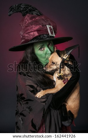 Halloween witch with green face and dog wearing wizard hat on red background