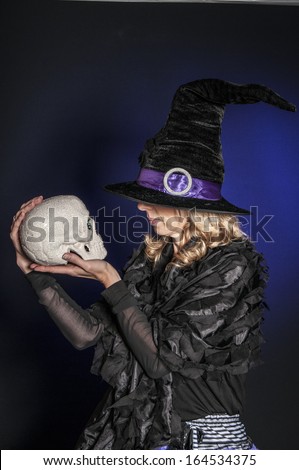 pretty woman dressed as Halloween witch holding a skull isolated on dark blue background