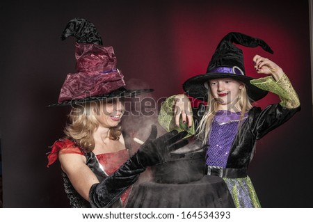 mother and daughter dressed as Halloween witches with cauldron isolated on dark red  background